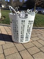 Photo of white plastic laundry hamper filled with many white plastic hangers outdoors on a paved area.