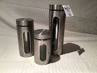 Three metal canisters with glass window, photographed together against neutral background.