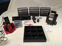 Photo showing the full assortment of office supplies including three metal mesh file organizers, red VTech phone, calculator, staplers, scissors, business card holder, pen storage unit with photos, small organizer tray, night light, and small accessories