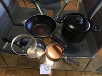 Photo showing the top view of the pots and pans on a glass table, including the pasta pot with lid, stir fry pan, egg pan, and sauce pan.