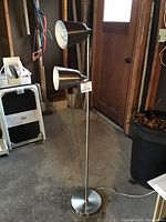 Full view of the floor lamp showing two cone-shaped adjustable lamps mounted on a vertical pole with a circular base in a workshop setting.