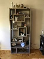 Full view of the tall shelving unit showing its multi-level compartments with various small decorative items displayed to illustrate use.