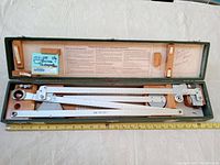 Pantograph instrument in green case, laid open showing full instrument and paper instructions on lid.