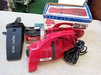 Red Dirt Devil Model 103 Hand Vac with original box, fabric dust bag, and long cord alongside a Black & Decker car vacuum and box of filter bags.