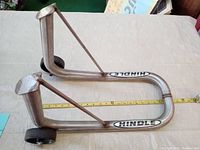 Side angled view of the Hindle metal wheel cart carrier with two wheels, showing the angled braces and Hindle decals, with measuring tape beside it for size reference.