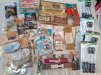 Full view of lot with door lock parts, brass door guard, nut locks, blades, saw handles, and miscellaneous hardware in packaging and loose