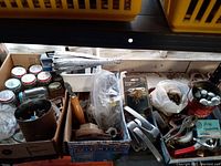 Photo showing assorted hardware items including packaged window lock, metal handles, pliers, screws in can, and other miscellaneous fastening pieces in containers and loose bags.