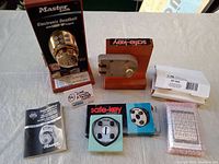 Master Lock electronic deadbolt with packaging and multiple Safe-Key mechanical locks with boxes and manuals on table.