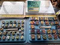 Two trays showing metal printers block stamps including uppercase alphabet letters and numbers, with two metal handles placed in the middle above a ruler for scale.
