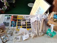 Photo of various vintage door locks, Hide-A-Key magnetic key cases, combo locks, telephone lock guard, and locksets arranged on a table.