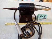 Front angle of vintage HR dual speed electric jewelry polishing grinder showing motor housing with attached conical grinding bit and connected handpiece with flexible cable, with measuring tape for scale.