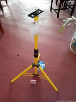 Full view of yellow tripod stand showing legs, height adjustment, and mounting plate.