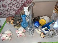 Photo shows an overall display of assorted ceramic and glass animal figurines along with vases and miniature cottages.