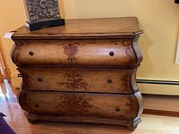 Frontal view of three drawer wooden dresser showing distressed paint and floral designs