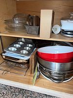 Metal 12-cup muffin tin and glass baking dishes stacked on shelf.