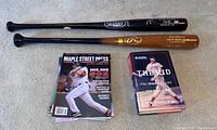 Photo of two wooden baseball bats and books and magazines laid on the floor