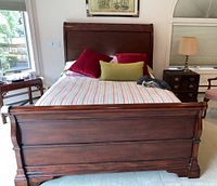 Front view of the wooden sleigh bed with mattress and pillows in a bedroom.