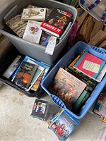 Three large storage boxes filled with a diverse collection of books, DVDs, and CDs on the floor and stacked.
