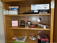 Photo of wooden shelf with multiple electronic items and boxes including Nook e-reader, Zune MP3 player box, Amazon Alexa devices, clock, chalk, and Synagy box.