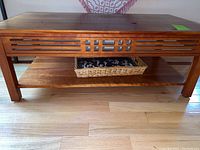 Front view of the wooden coffee table showing the rectangular top, carved linear apron, lower shelf, and wicker basket inside.