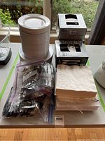 Photo showing stacks of small and large white disposable plates, boxes of disposable plastic cutlery, and stacks of white napkins on table.