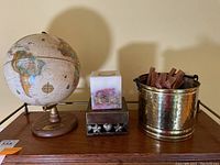 Vintage globe displayed on a wooden surface alongside brass bucket with incense sticks and a decorative candle holder.