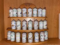 Full view of the three-tier wooden spice carousel holding 23 ceramic spice jars arranged in rows with decorative painted designs on each jar.