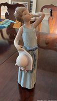 Front and side view of Lladro figurine showing a girl in a blue dress holding a pink hat.