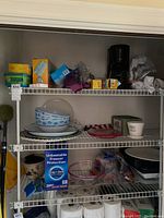 Shelf with assorted plastic bowls, serving platters, food storage containers, and black drip coffee maker.