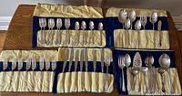 Full view of the flatware items arranged in yellow and blue fabric rolls, showing forks, knives, spoons and serving utensils