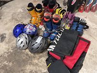 Photo of three pairs of alpine ski boots (yellow Salomon, red Nordica, blue Lange), four pairs of cross-country ski boots, and four youth helmets.