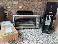 Wide shot of SodaStream carbonator next to Breville toaster oven on granite counter showing box with CO2 refill cylinders.