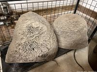 Two speaker rocks with natural rock-like design placed side by side on a floor, triangular and rounded shapes visible