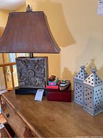 Tall table lamp with raised acorn motif base and shade next to two silver metal star cutout lanterns on wooden dresser.