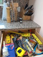 Photo showing an open drawer filled with assorted household tools: tape measure, hammers, pliers, screwdriver, paint brush, level, utility knives.