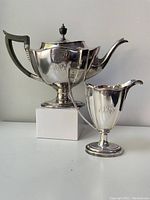 Teapot and milk jug shown side by side with engraved monogram visible on both.