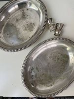 Two oval silver plated serving dishes with beaded trim, showing tarnish and patina, alongside a pair of small matching silver plated salt and pepper shakers.
