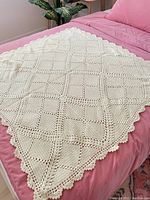 Full view of cream crochet blanket on bed showing diamond stitch pattern and scalloped edges