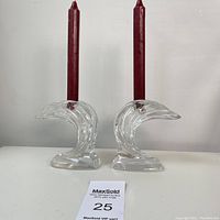 Pair of clear crystal candle holders shaped like ocean waves with red tapered candles inserted, shown side by side on a white background.