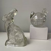 Photo showing both glass items: a clear glass rabbit candy container and the Anchor Hocking hen on nest glass dish with lid, placed on a white background.