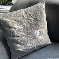 Full view of the embroidered cushion placed on a chair showing overall pattern and condition.