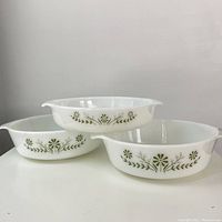 Three Glasbake 438 USA milkglass ovenware dishes with green daisy primrose floral design shown stacked, to display decorative sides and handles.