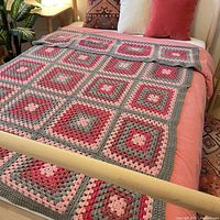 Full view of the granny square afghan spread on a double/full bed, displaying the color pattern and square arrangement.