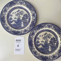 Pair of English Ironstone Blue Willow plates displayed flat on surface, showing full front design and size comparison against auction card.