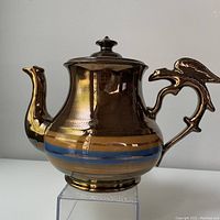 Copper lustreware griffin teapot front view showing cobalt band and raised details on body with griffin-shaped handle.