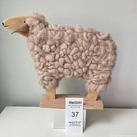 Front view of the wooden toy sheep showing curly wool body, wooden head and base, with leather neck detail.