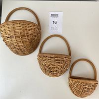 All three wicker wall pocket baskets on a flat white surface, laid side by side showing their varying sizes and the woven wicker texture.