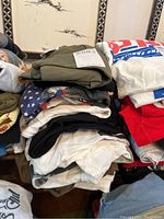 Stack of folded Beatles t-shirts in various colors and sizes, placed on furniture.