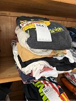 Stack of folded Beatles-themed T-shirts on wooden shelf, showing assorted colors and prints.