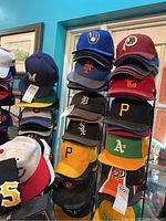 Wide angle showing multiple stacks of sports caps including several MLB and NFL teams on display rack.